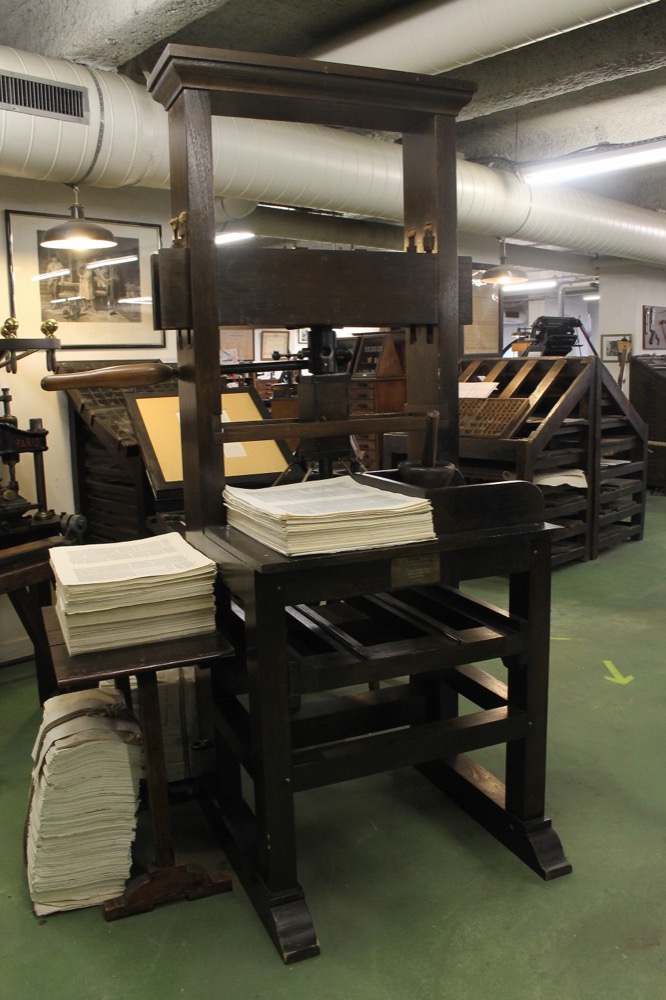 A wooden hand press with stacks of printed sheets, in a printing museum
