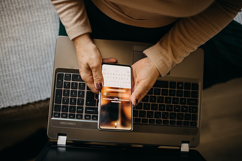 Hands holding a phone over an open laptop