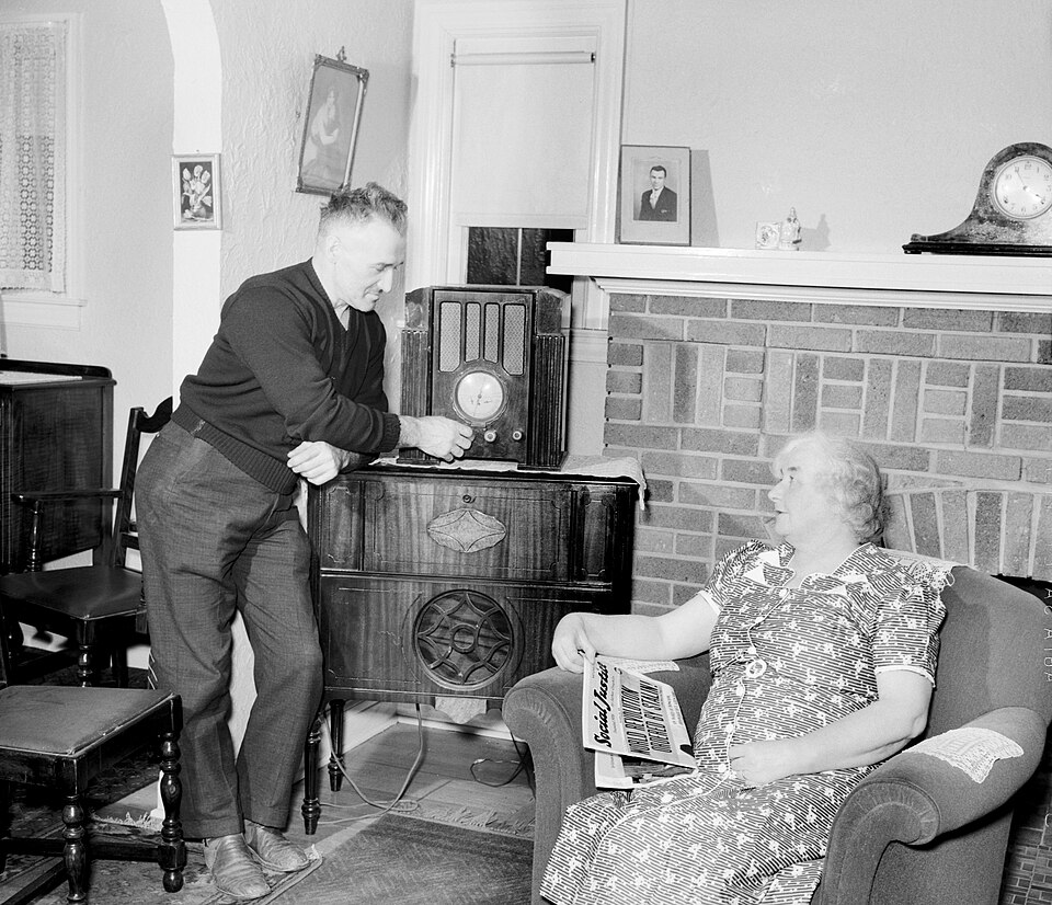 A couple at home next to a large radio set